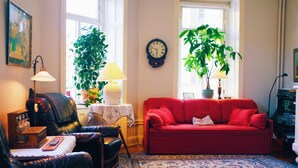 A cozy living room with a red sofa, a black leather armchair, a wooden side table with a lamp, and two potted plants.