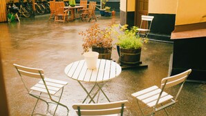 A wet outdoor patio area with a round table and two chairs, surrounded by potted plants and a row of bicycles in the background.