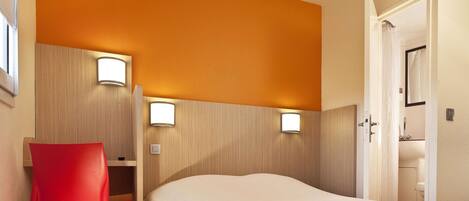 A hotel room with a bed, a red chair, and two wall-mounted lights.
