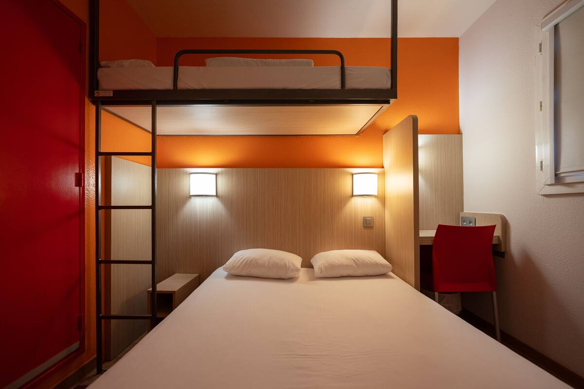 Une chambre avec un lit superposé doté d’une tête de lit en bois, un bureau avec une chaise et une porte rouge.