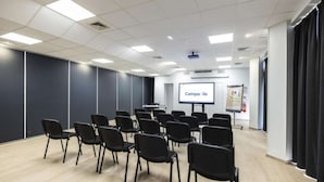 Une salle de conférence avec des rangées de chaises noires, un écran de projection affichant le mot « Campanile » et un tableau blanc.