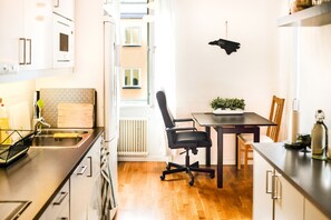 A compact kitchen with a dining area, a radiator, and a window with a view of buildings. - Comfortable Studio Apartment - Midsommarkransen (Hägersten)