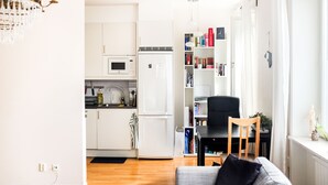 Une cuisine moderne avec des meubles blancs, un four à micro-ondes et un réfrigérateur. On y trouve également un coin repas avec une chaise noire et une bibliothèque remplie de livres.