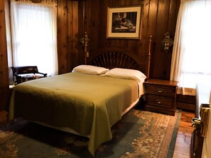 A wooden-paneled bedroom with a bed, a nightstand, a chair, and a framed picture on the wall. - Wauban Cottage (Northport)