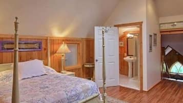 A bedroom with a four-poster bed, wooden walls, a window, and a door leading to a bathroom.