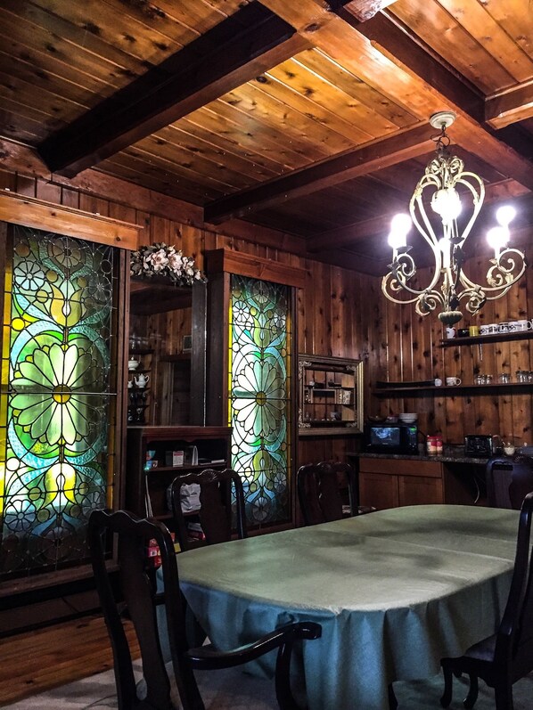 A wooden interior with a dining table, chairs, a chandelier, and stained glass windows. - Wauban Cottage (Northport)