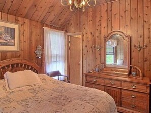 A wooden-paneled room with a bed, a dresser, and a mirror. - Wauban Cottage (Northport)