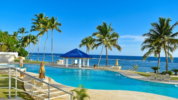 A pool area with a blue-roofed pavilion, palm trees, and a view of the ocean. - Las Olas by Destinos 1A (Guayacanes)