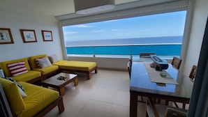 A balcony with a view of the ocean, a yellow sofa, a dining table, and a small table with a cup and saucer. - Las Olas by Destinos 1A (Guayacanes)