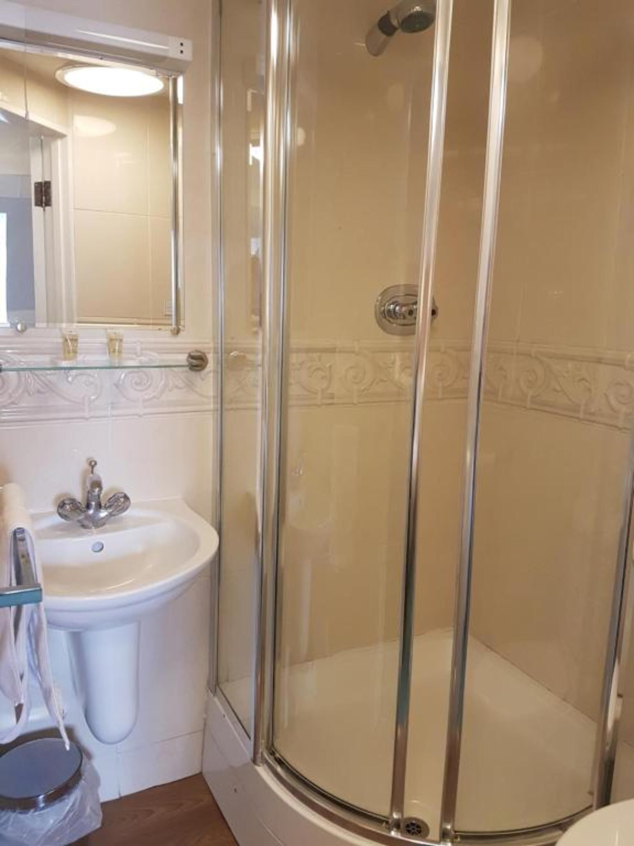 Une salle de bain avec une douche à parois de verre, un lavabo sur colonne et un miroir au-dessus du lavabo.