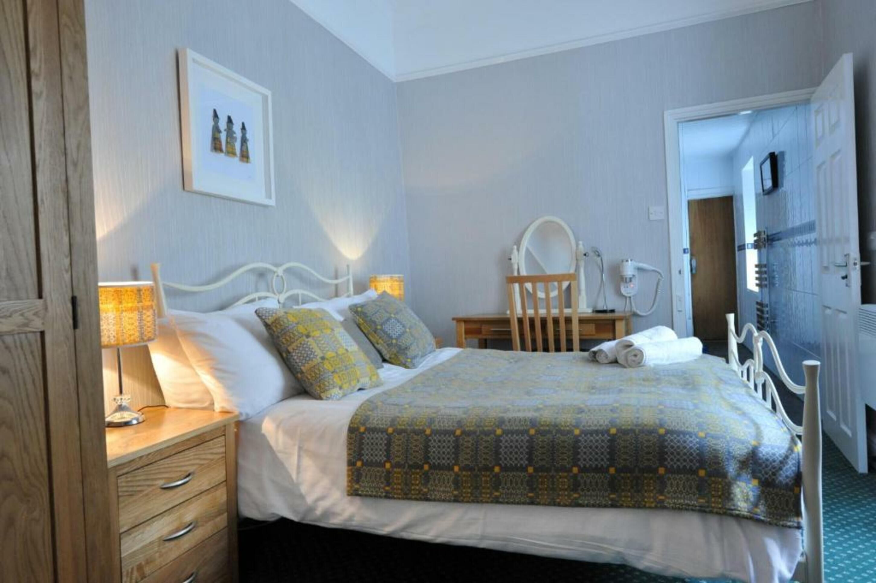 A bedroom with a bed, bedside table, lamp, and a mirror.