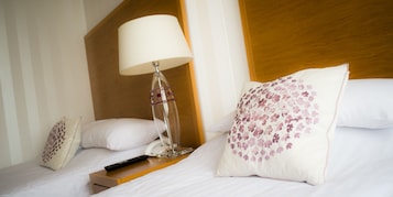 Un letto rifatto con lenzuola bianche, un telecomando, una lampada e cuscini decorativi.
