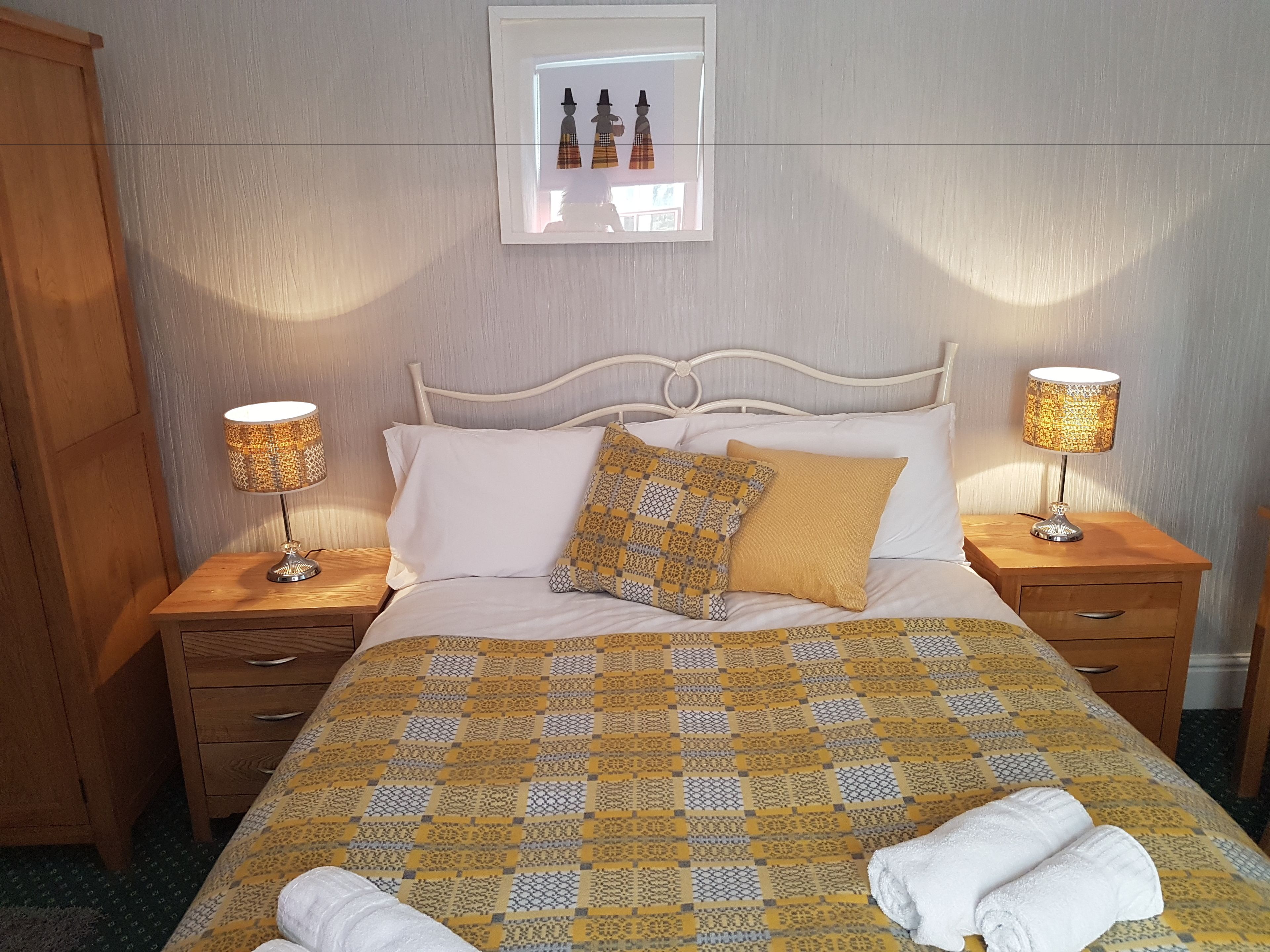 A neatly made bed with a patterned bedspread, two bedside lamps, and a framed picture above the bed.