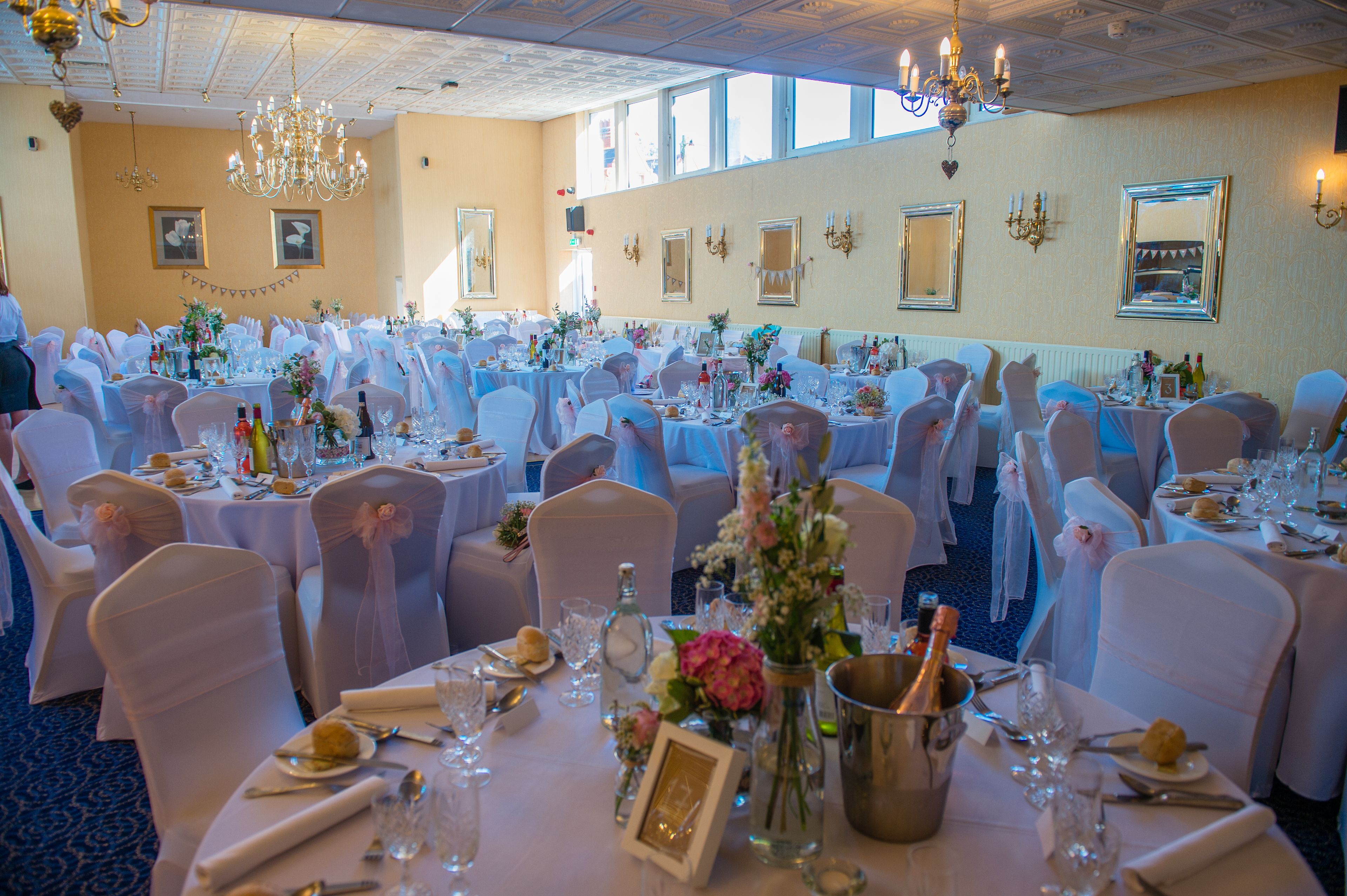 A banquet hall with round tables, white tablecloths, and chairs with white covers.