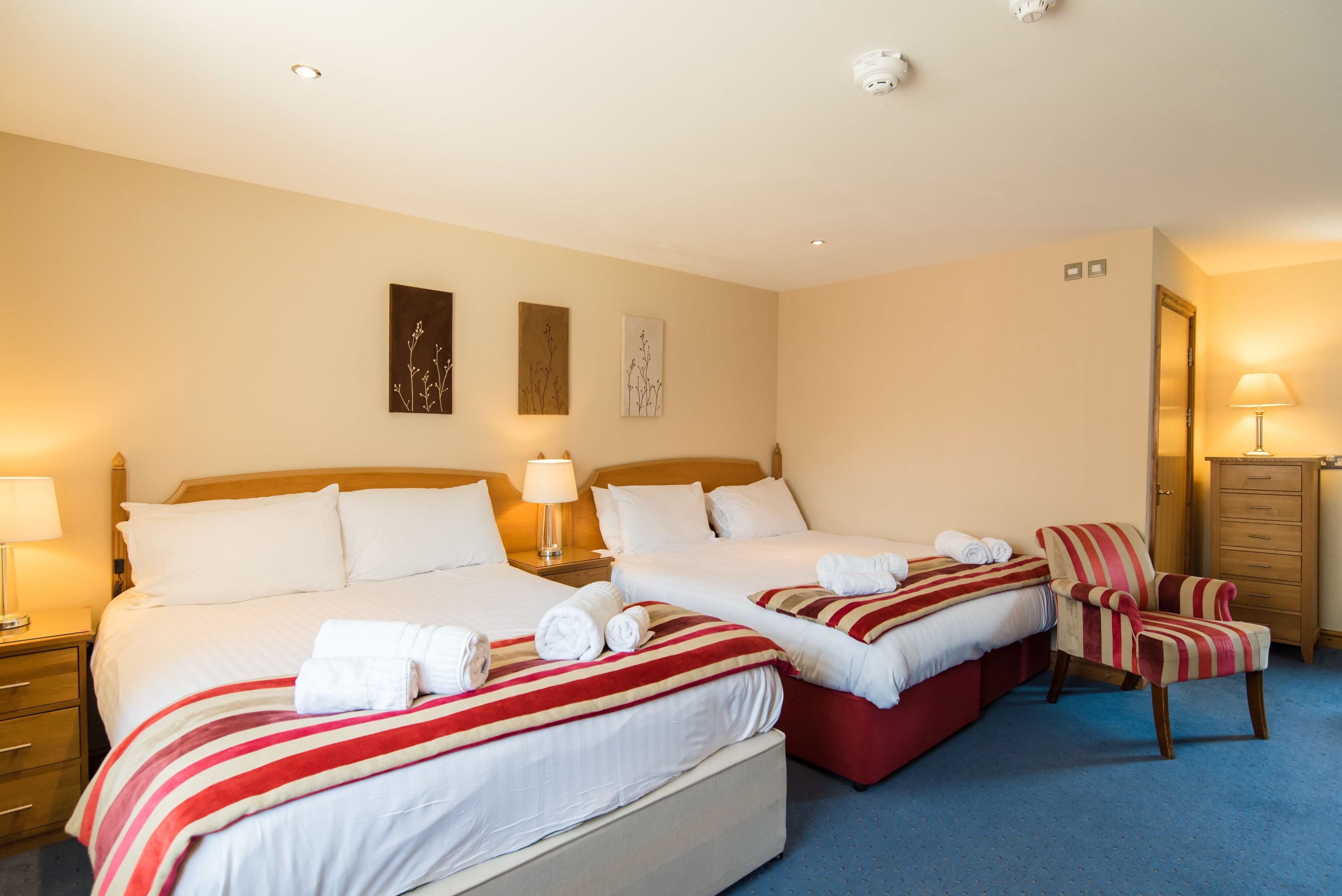 A hotel room with two beds, a chair, a nightstand, and a lamp.