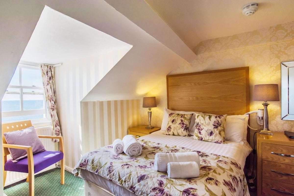 A hotel room with a bed, a chair, a nightstand, a lamp, and a window with curtains.