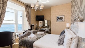 A hotel room with a bed, a desk, a chair, a TV, and a view of the sea. - Gwesty'r Marine Hotel & Spa (Aberystwyth)