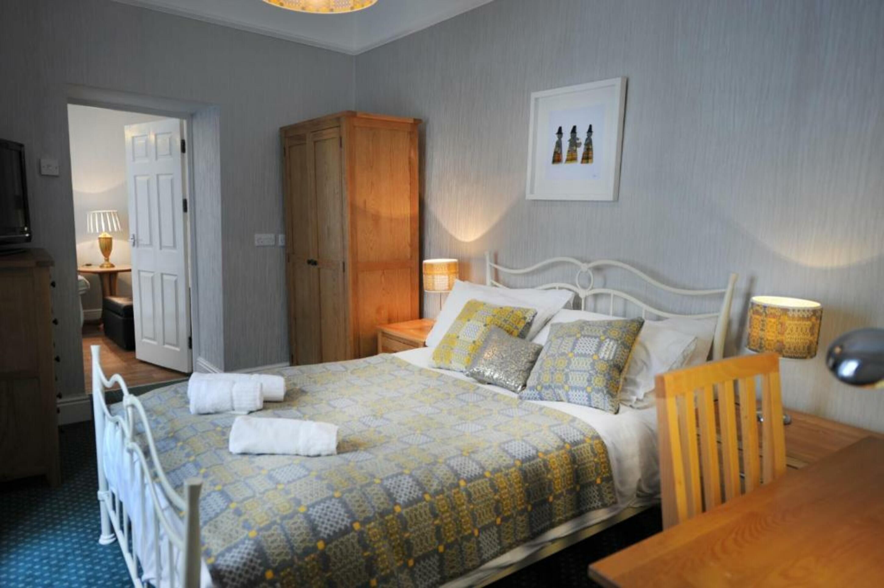 Une chambre à coucher bien rangée, avec un lit, des tables de chevet, une armoire en bois et un tableau encadré accroché au mur.