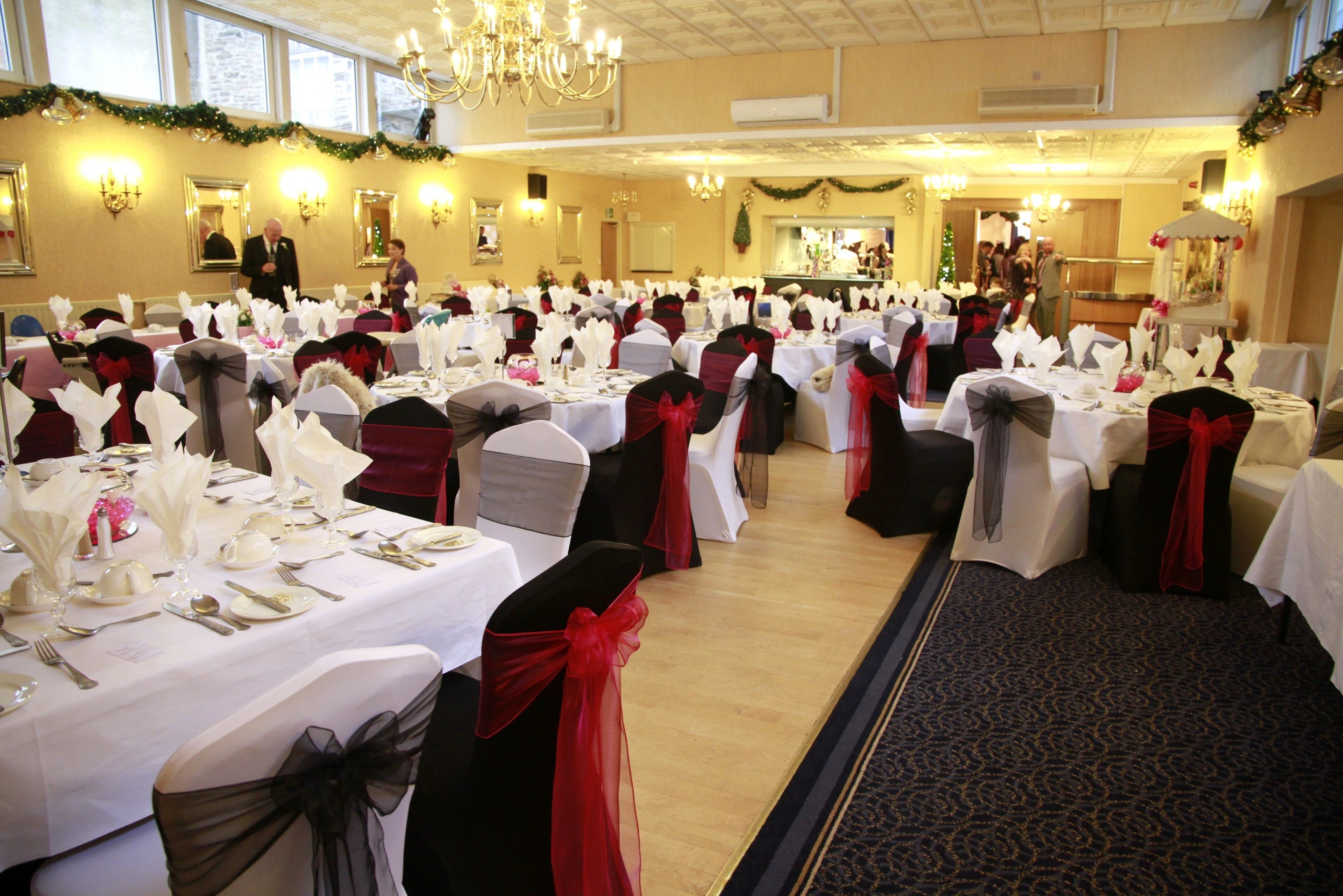 A banquet hall with tables set for a formal event, featuring white tablecloths and red sashes.