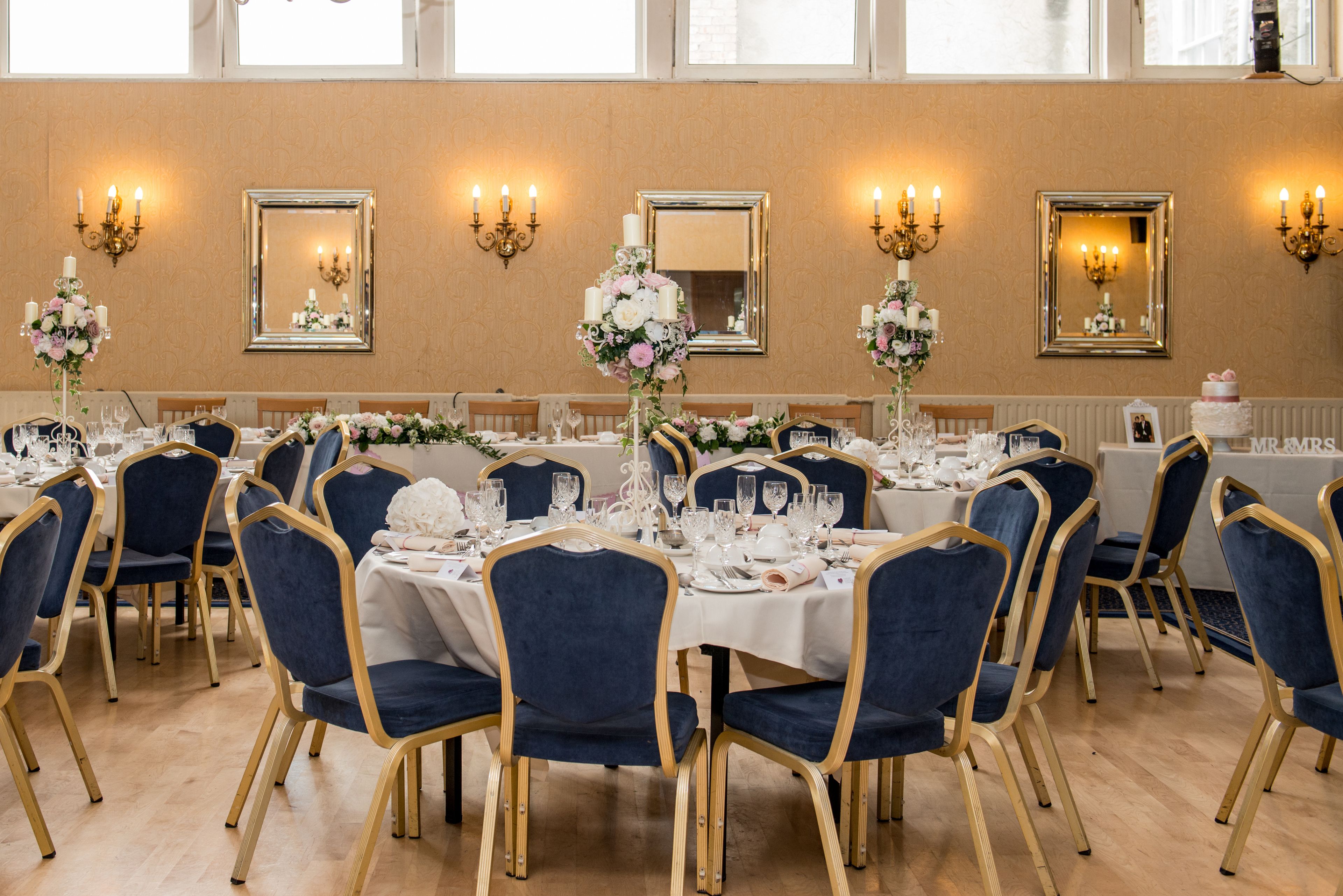 Een balzaal met ronde tafels, blauwe stoelen en bloemrijke decoraties.