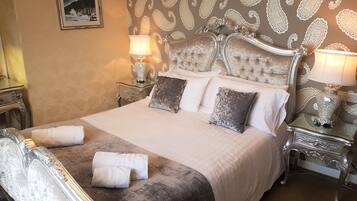 Un letto grande con testiera trapuntata, due comodini con lampade e carta da parati decorata.