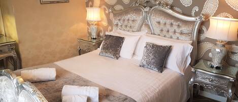 A large bed with a tufted headboard, two bedside tables with lamps, and a patterned wallpaper.