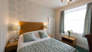 A hotel room with a large bed, two bedside tables with lamps, a wooden headboard, a window with curtains, and a chandelier.