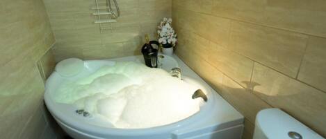 A bathroom with a large bathtub, a toilet, and a shower area.