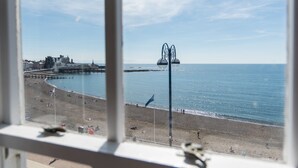 A beach view through a window, including a pier and a flagpole. - Gwesty'r Marine Hotel & Spa (Aberystwyth)