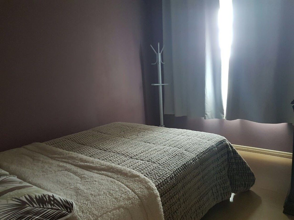 Een slaapkamer met een bed, een kapstok en een raam met gordijnen.