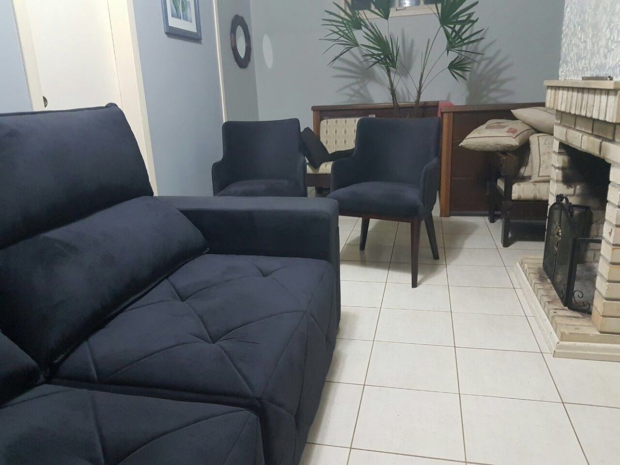 A living room with a dark-colored sofa, two armchairs, a small table, and a fireplace.