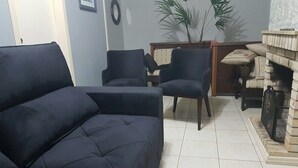 Una sala de estar con un sofá de color oscuro, dos sillones, una mesita y una chimenea.