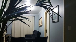 Una habitación con una mesa de comedor y sillas, un sofá, una planta grande y cuadros en la pared.