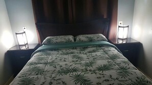 Una cama con colcha estampada, dos mesitas de noche y un velador con lámpara.