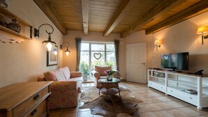 Una sala de estar acogedora con techo de madera, un sofá, una mesa de centro y un televisor sobre un mueble blanco.