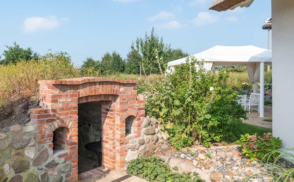 Un four extérieur en briques, un gazebo blanc et un jardin agrémenté de diverses plantes.