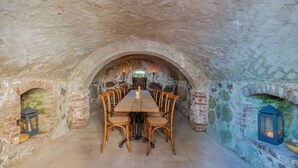 A rustic dining area with a long table and wooden chairs, stone walls, and a small fireplace. - Lerchenhof Reestow (Rankwitz)