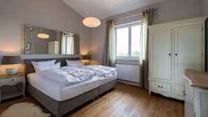 A bedroom with a large bed, bedside lamps, a dresser, and a window with curtains. - Lerchenhof Reestow (Rankwitz)