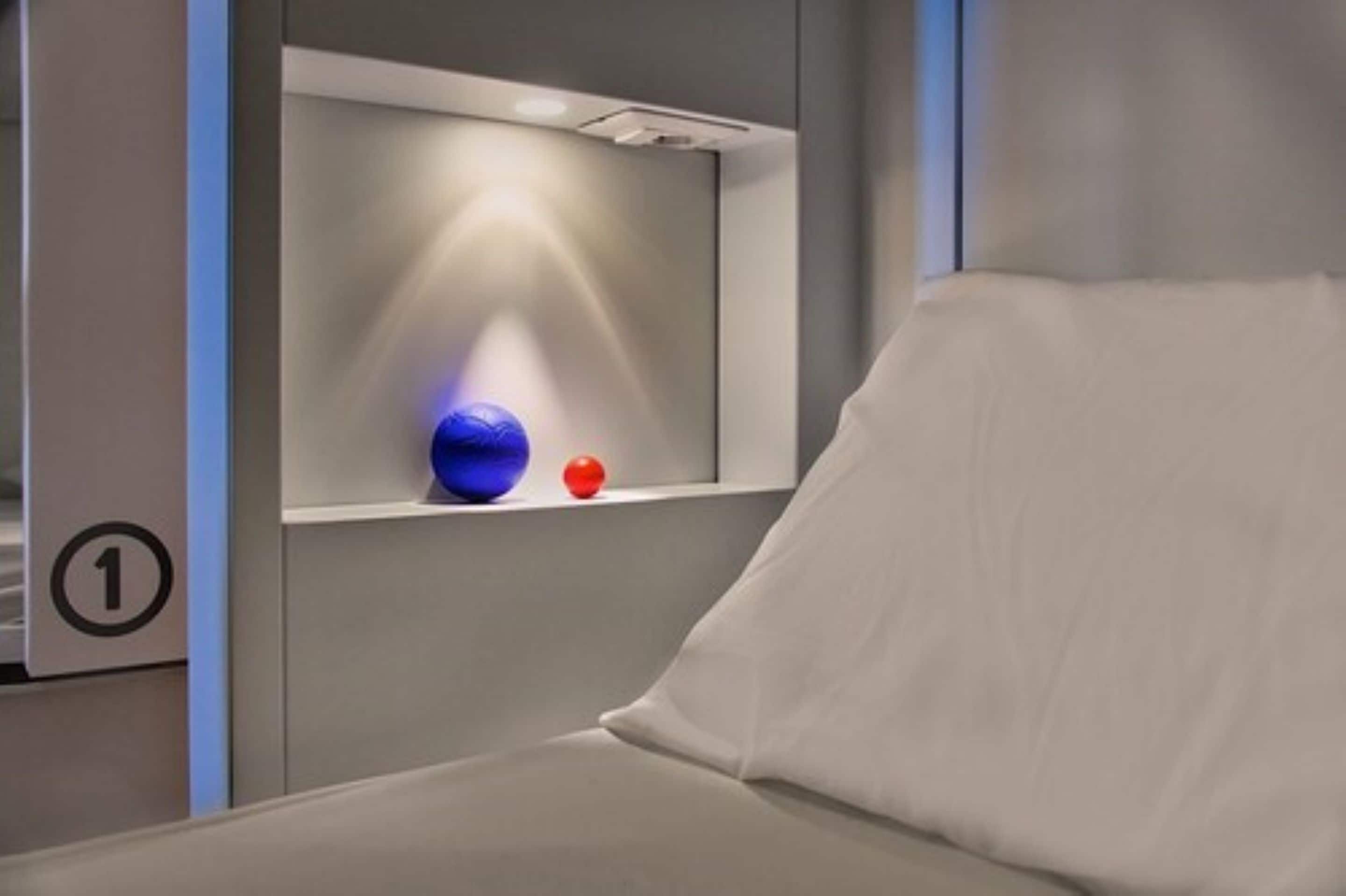A modern hotel room with a white bed, a shelf with decorative items, and a number indicating the room.