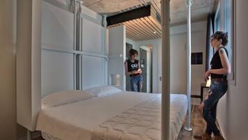 A modern bedroom with a large bed, a wooden floor, and a high ceiling with exposed beams.