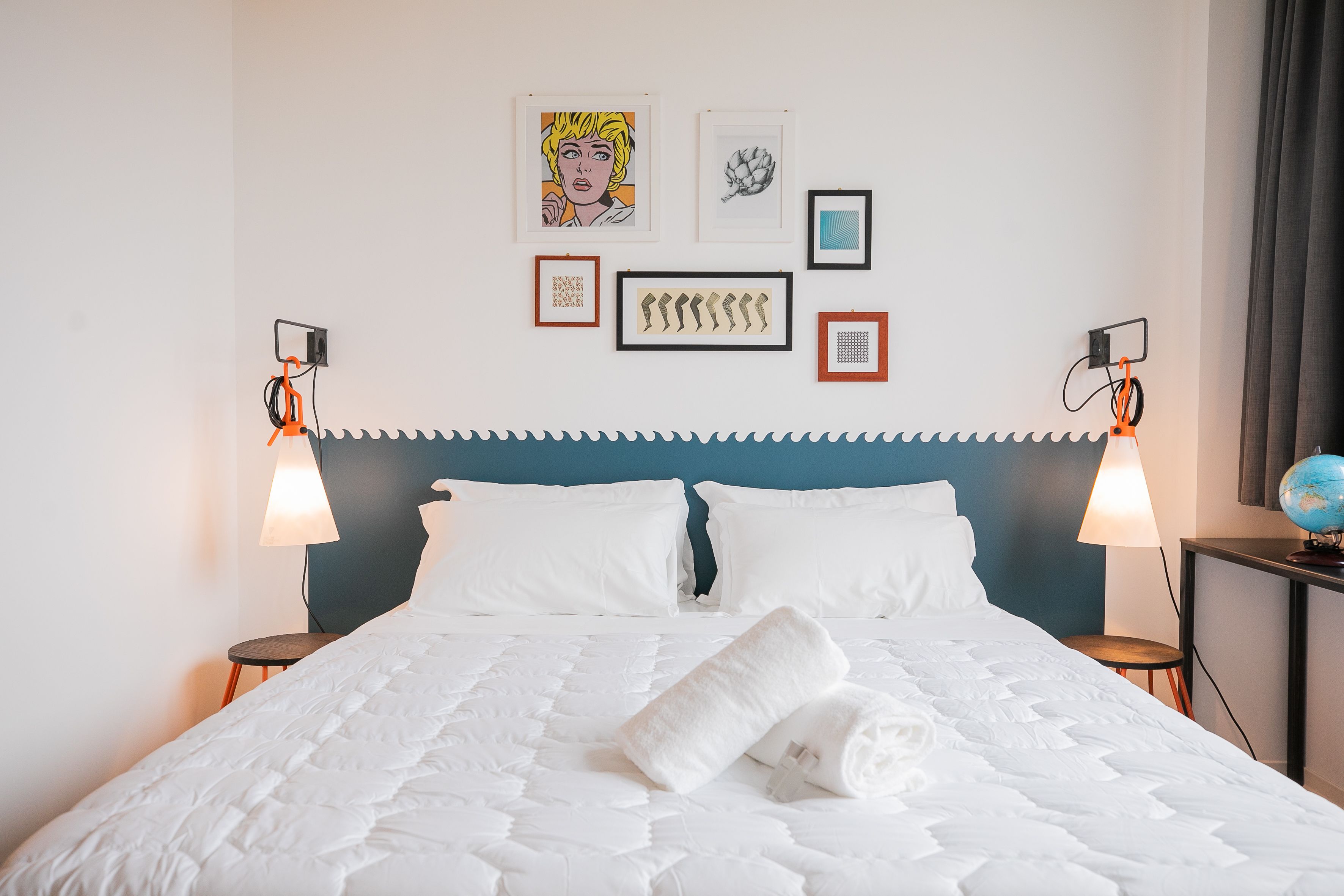 Una cama bien hecha con ropa blanca, un cabecero azul y cuadros en la pared.