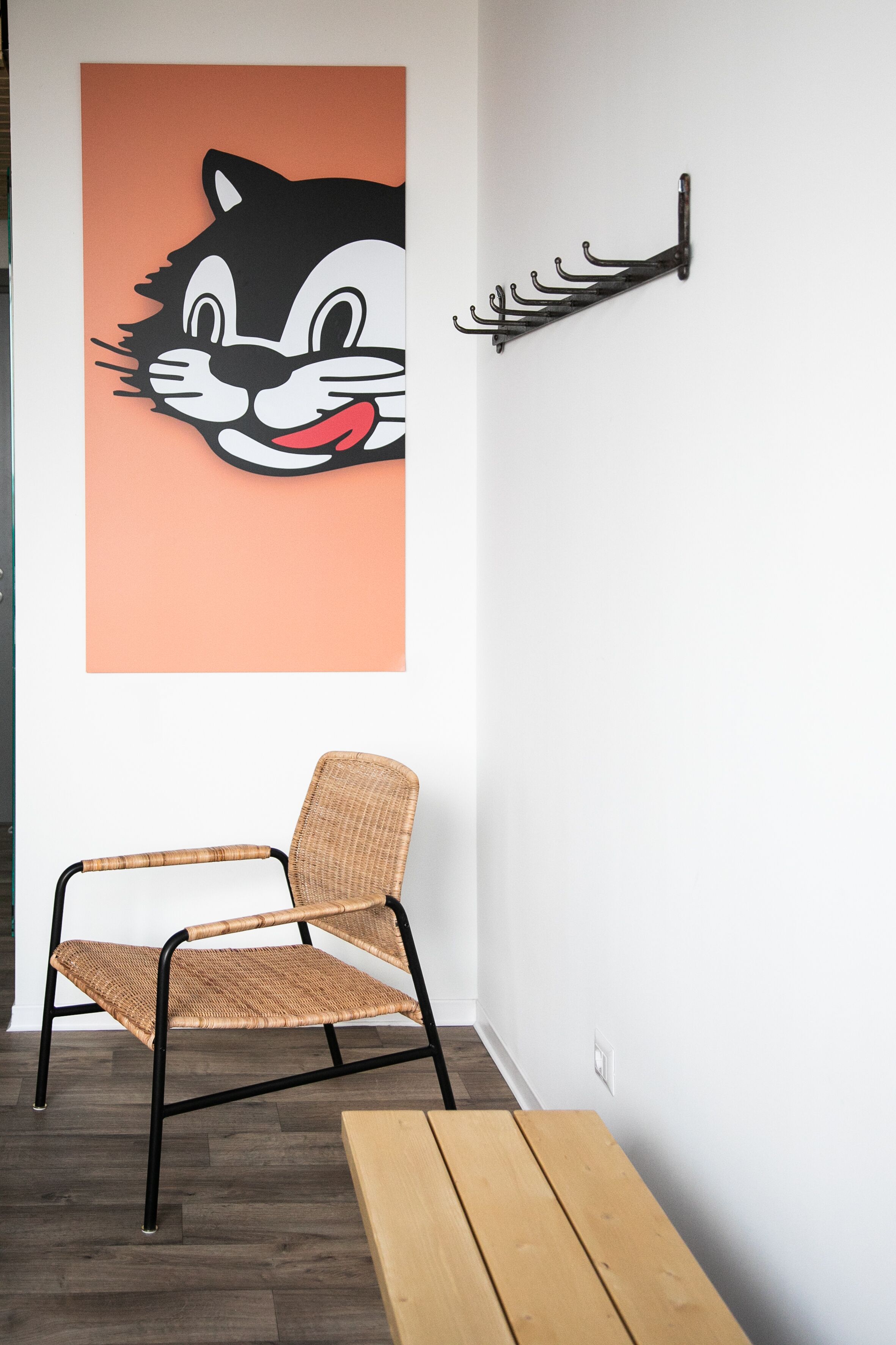 A room with a wicker chair, a wooden bench, and a wall-mounted coat rack.