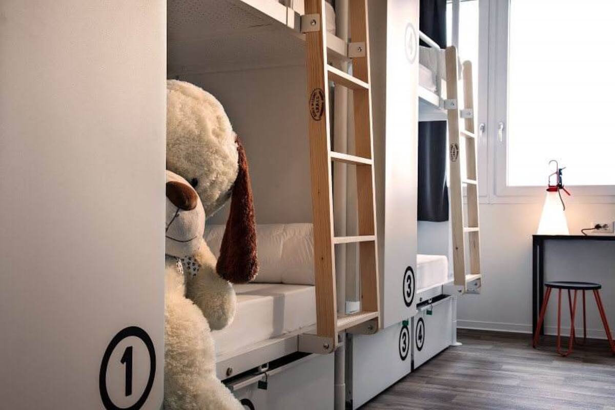 A bunk bed with a built-in desk and shelving, a teddy bear, and a lamp on a table.
