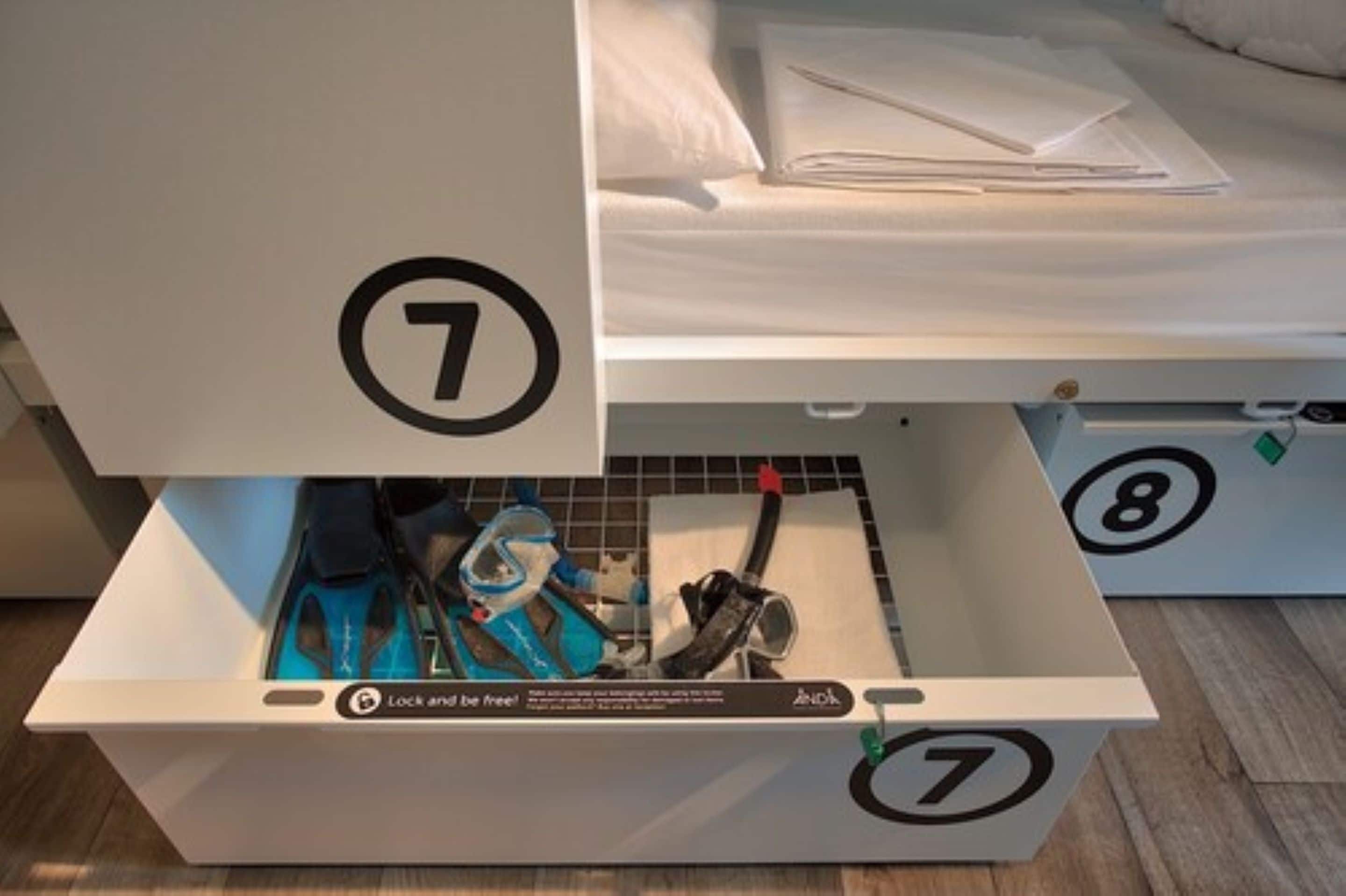 A storage box with a lock and key, containing various items including a blue bag and a white pillow.