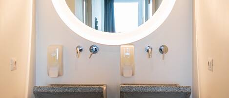 Un baño moderno con dos lavamanos de granito, un espejo redondo y techo de madera.