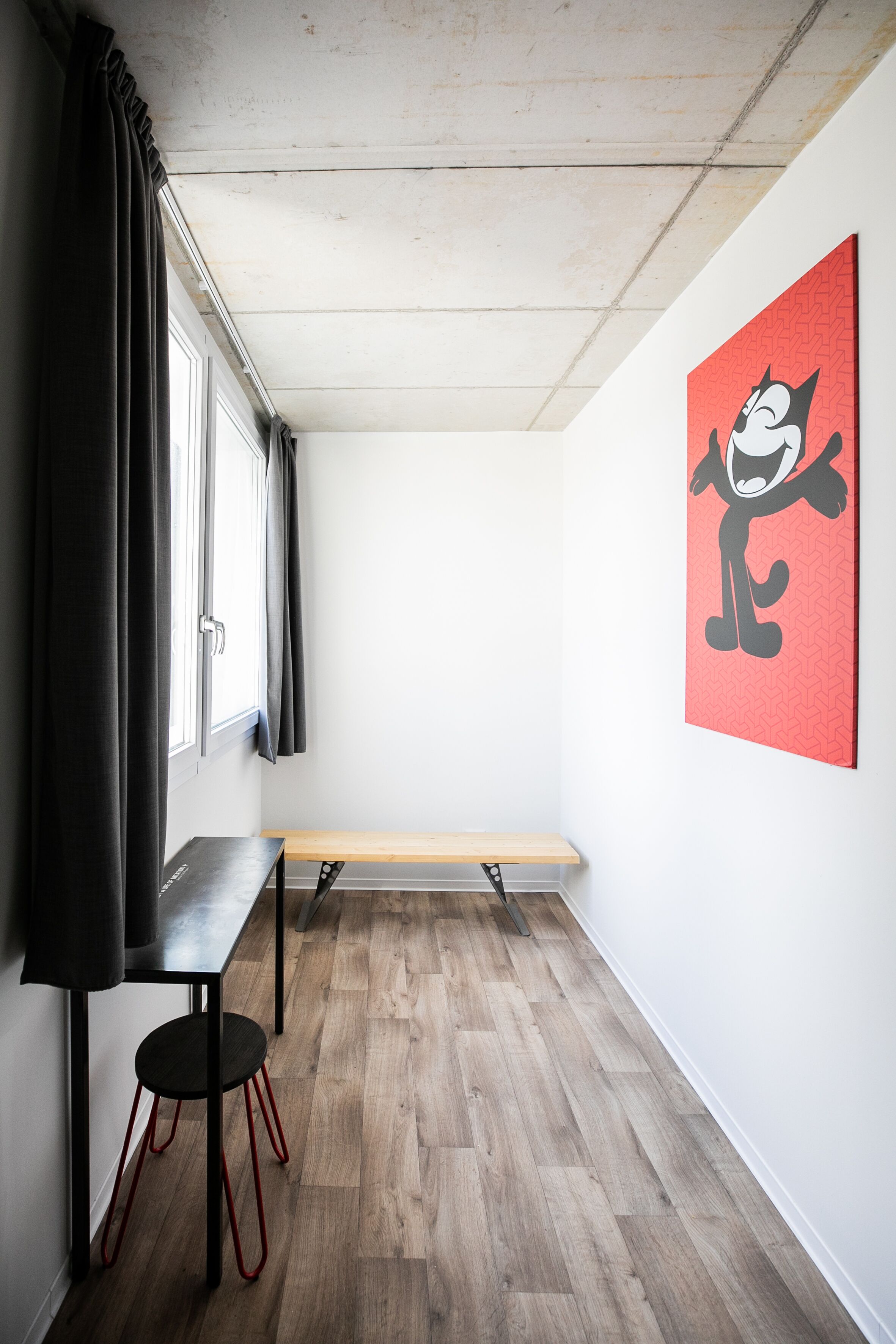 A room with a wooden floor, a black table with red legs, a bench, and a red and black artwork on the wall.