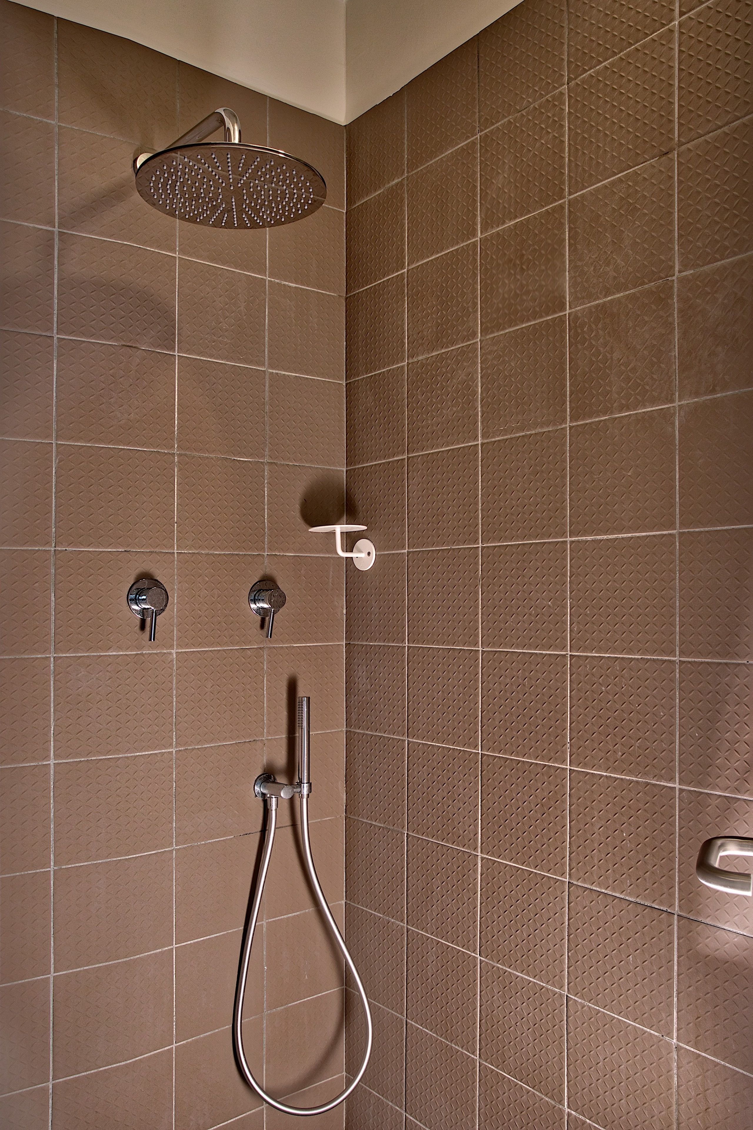 A shower area with a handheld showerhead, a wall-mounted faucet, and a handheld shower hose.