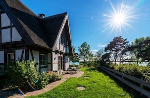 A traditional half-timbered house with a thatched roof, a paved pathway, and a wooden fence.