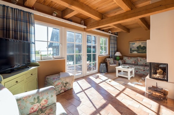 A cozy living room with a fireplace, floral sofas, a television, and large windows.