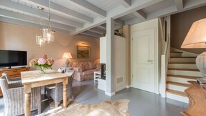 A spacious living room with a wooden dining table, wicker chairs, a sofa, and a television. A staircase is visible in the background. - Bauernkate Liepe (Rankwitz)